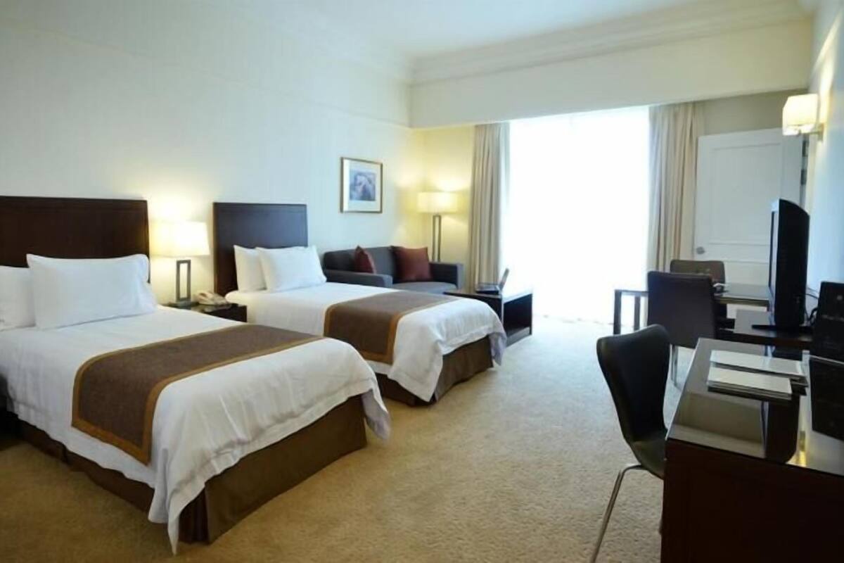 Una habitación de hotel con dos camas, un escritorio, una silla, un televisor y una ventana.