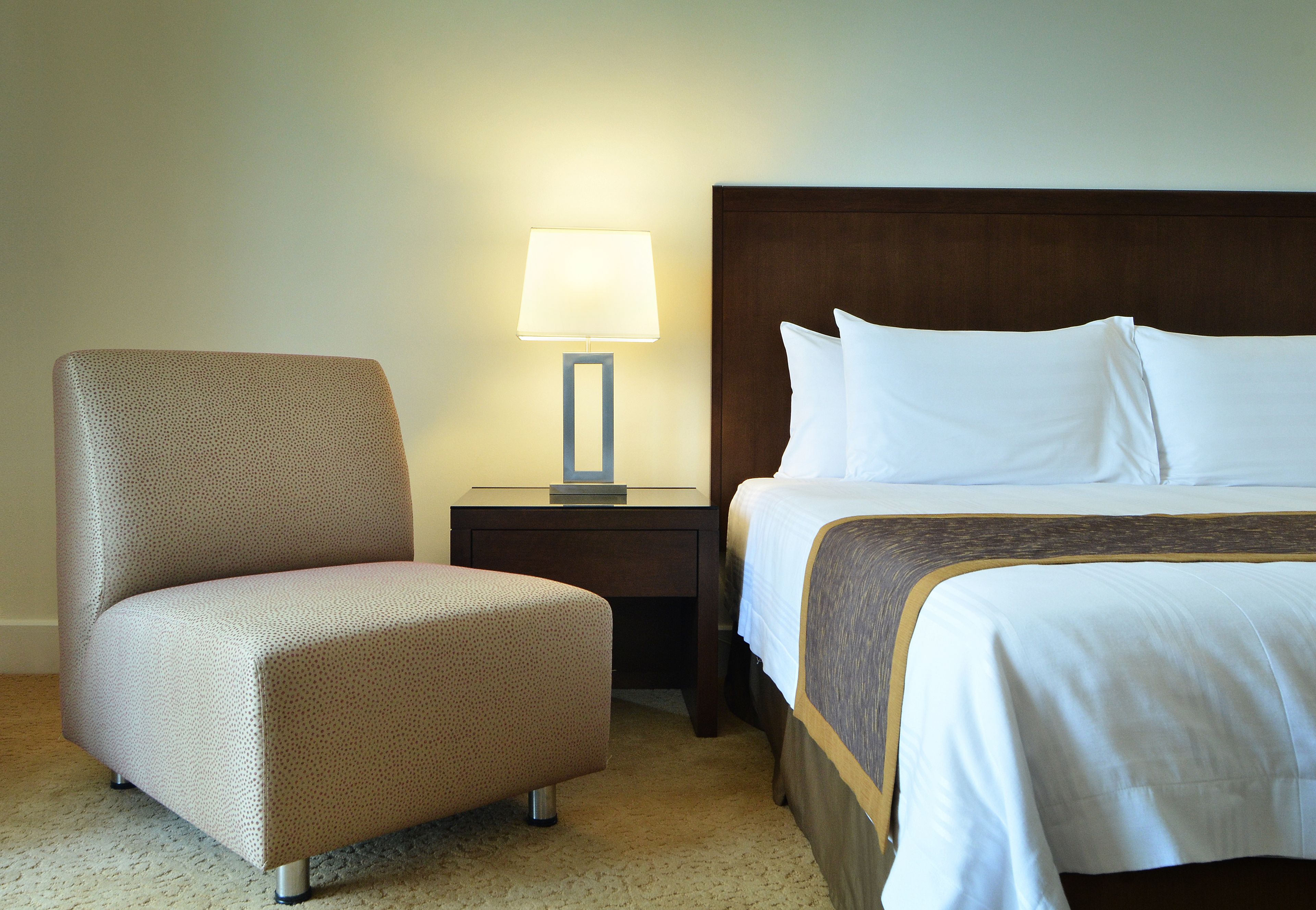 A hotel room with a bed, a chair, and a nightstand with a lamp.
