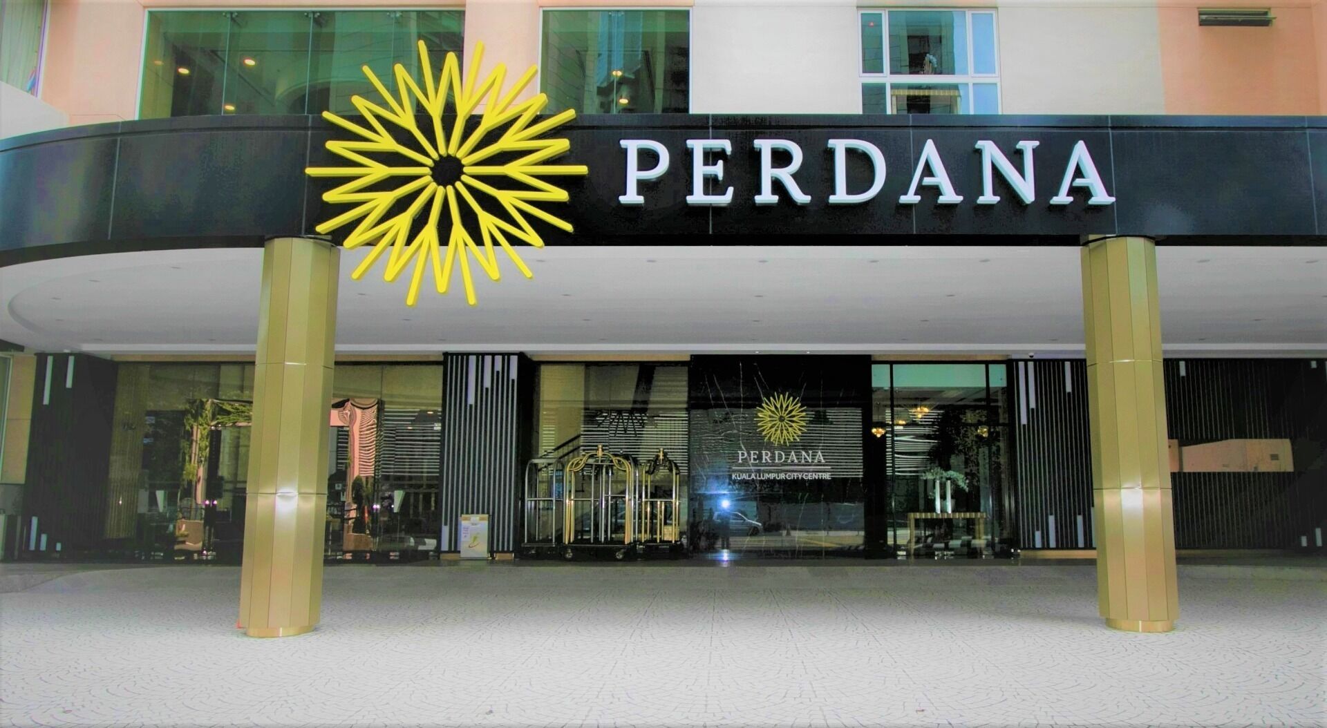 L’extérieur d’un hôtel appelé « PERDANA », qui se distingue par son logo en forme de soleil et son entrée moderne.