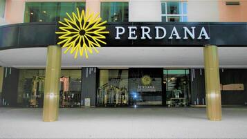 The exterior of a hotel named 'PERDANA' with a prominent sun-like logo and a modern entrance.