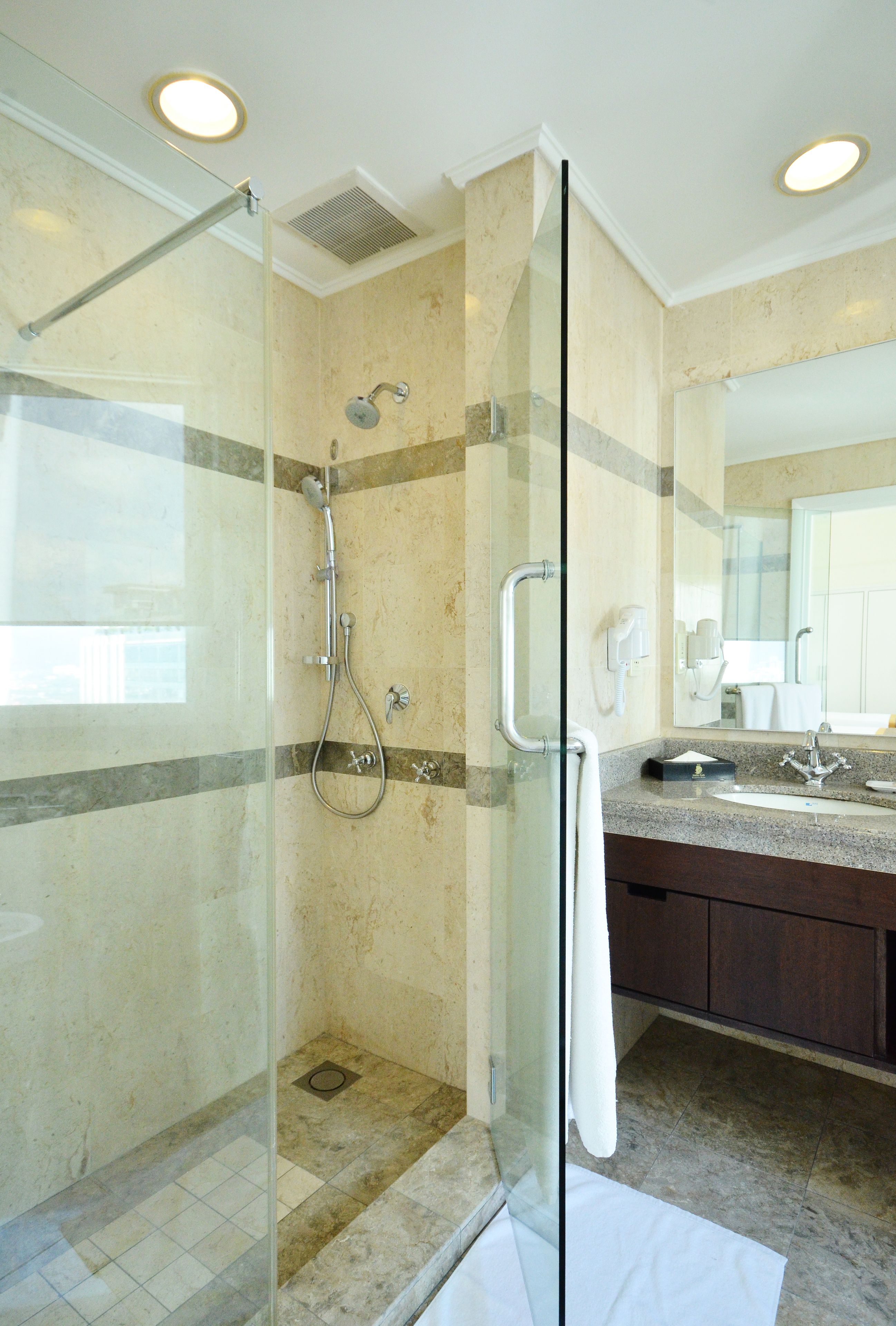 Un baño moderno con ducha de vidrio, un espejo grande y suelo de mármol.