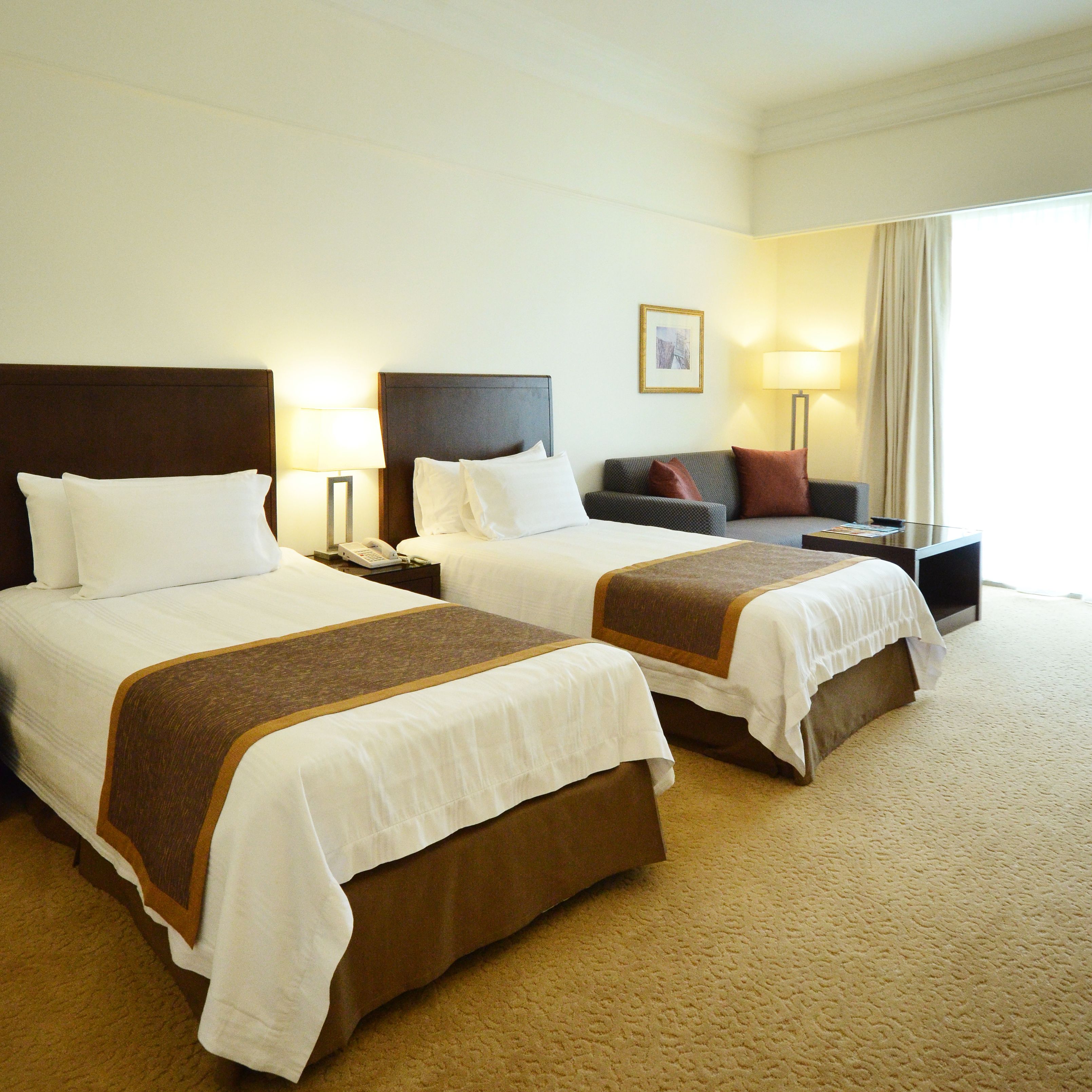 A hotel room with two beds, a sofa, a desk, and a lamp.