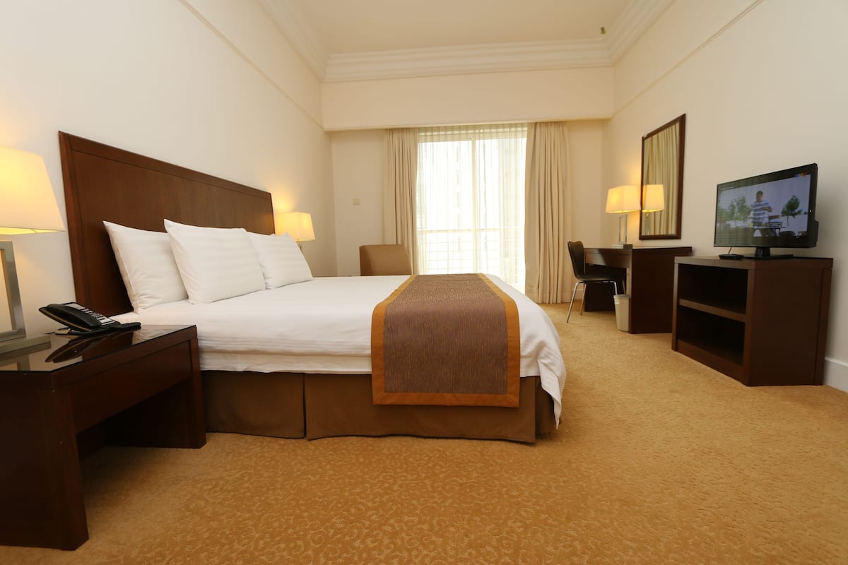 A hotel room with a large bed, a desk with a lamp, a television, and a chair.