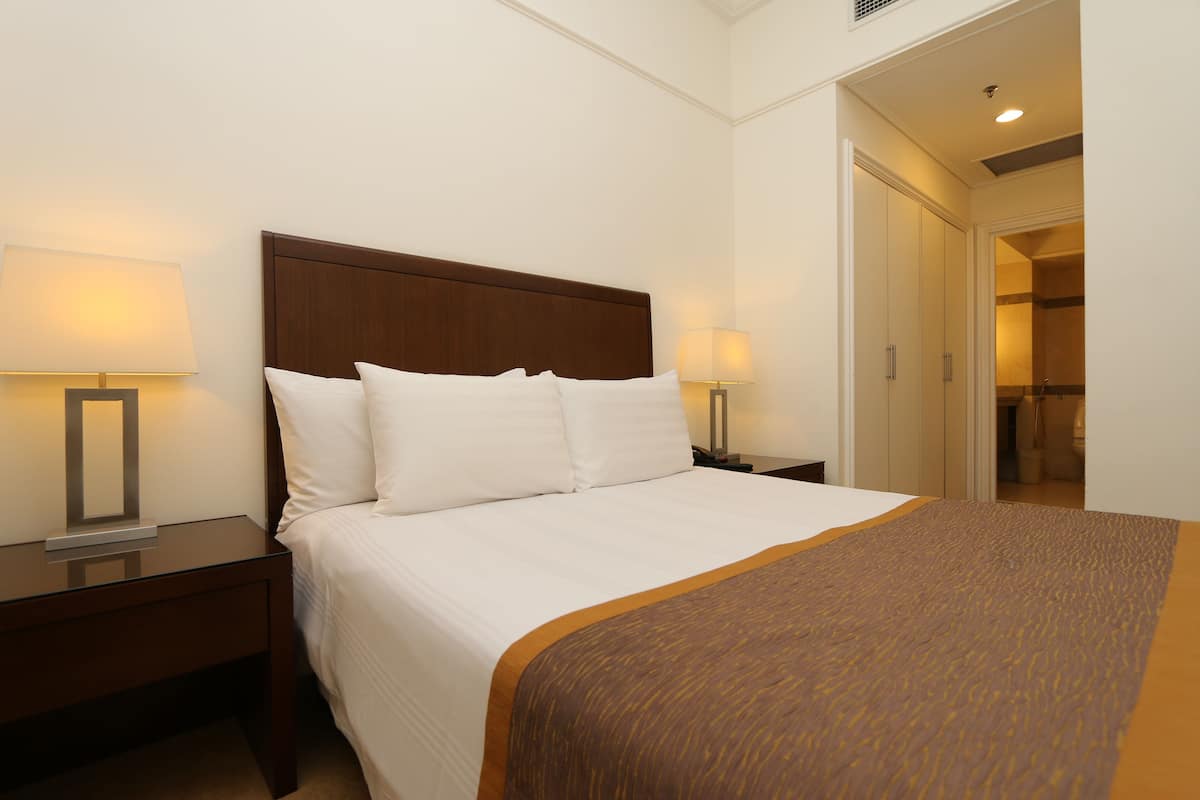 A neatly made bed with white linens and a brown accent, flanked by two bedside tables with lamps, in a hotel room with a simple, clean design.