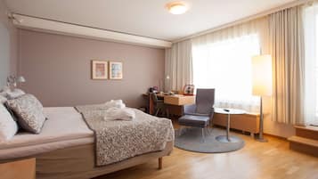 A hotel room with a bed, desk, chair, and a lamp.
