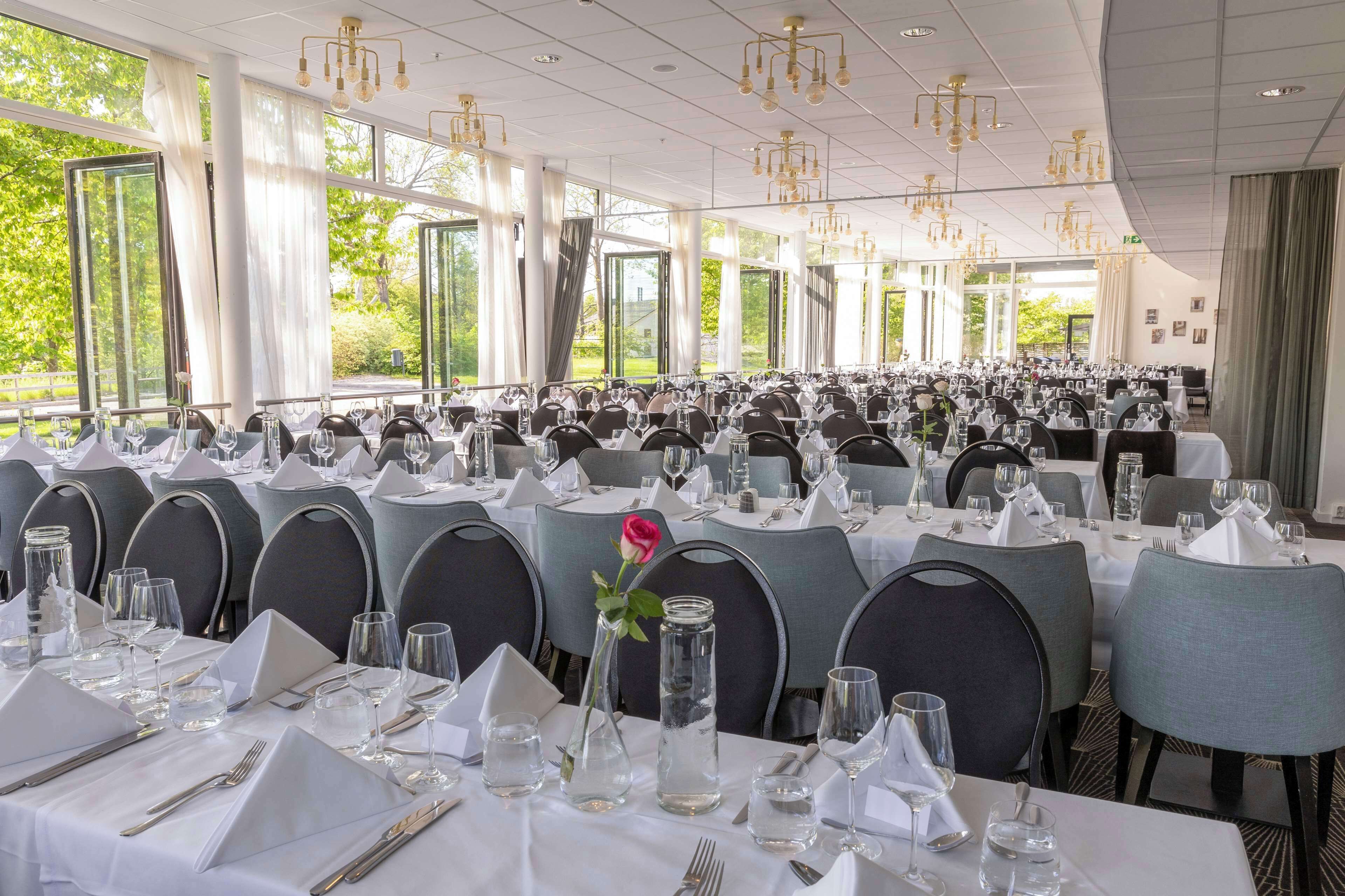 Un salón de banquetes con mesas dispuestas para un evento formal, amplias ventanas y candelabros.