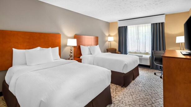 A hotel room with two beds, a desk, a chair, and a television.
