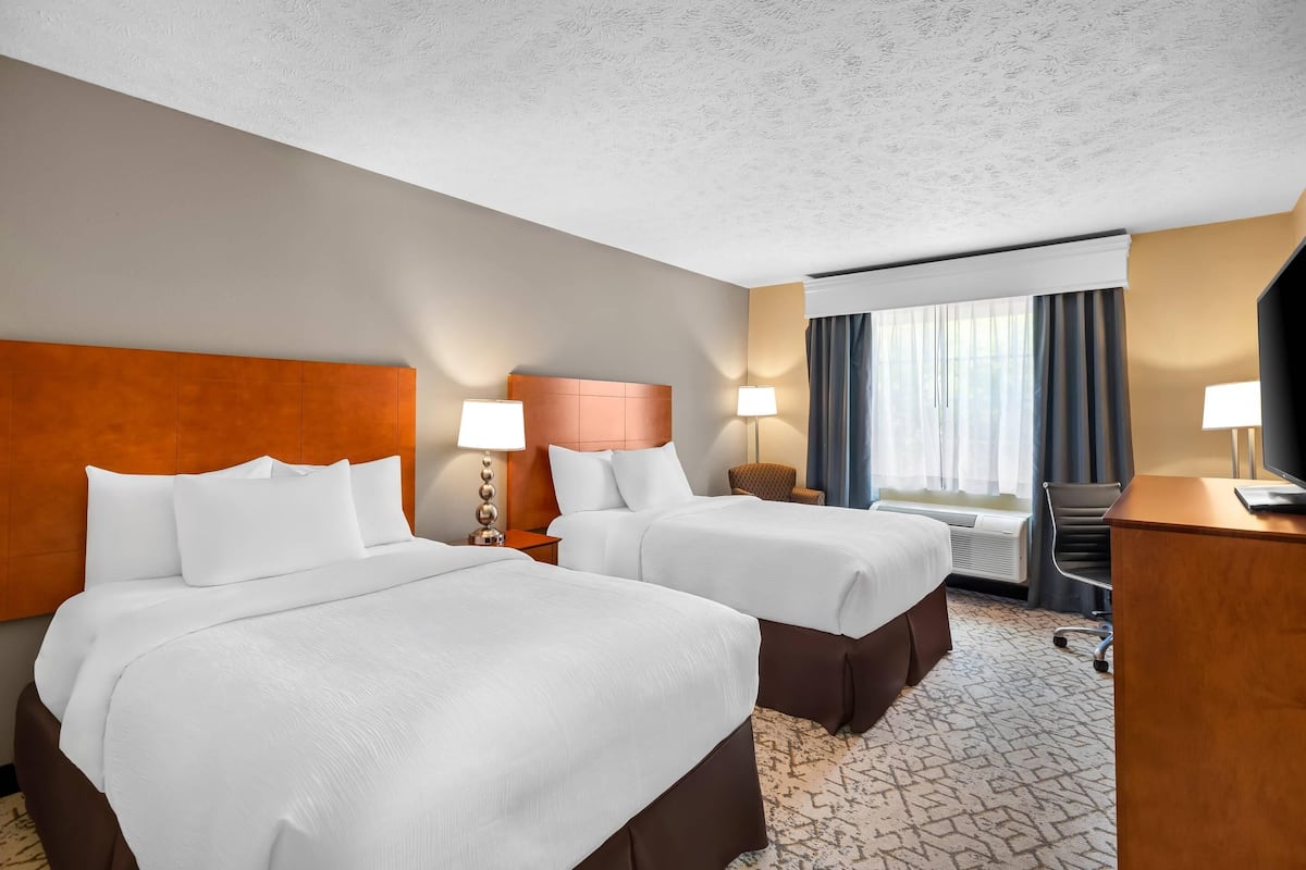 A hotel room with two beds, a desk, a chair, and a television.