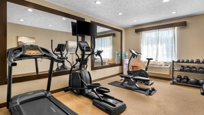 A hotel gym with treadmills, an elliptical, a stationary bike, and a rack of dumbbells.