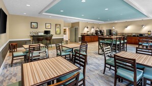 A restaurant with multiple tables and chairs, a kitchen area, and a ceiling with recessed lighting.