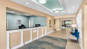 A hotel reception area with a counter, a sign reading 'Quality by Chuck Hotel,' a reception desk, a blue wall, and a hallway leading to other rooms.