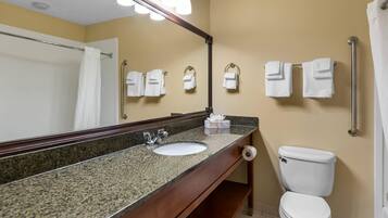 A bathroom with a granite countertop sink, a mirror, a white toilet, and a towel rack with multiple towels.
