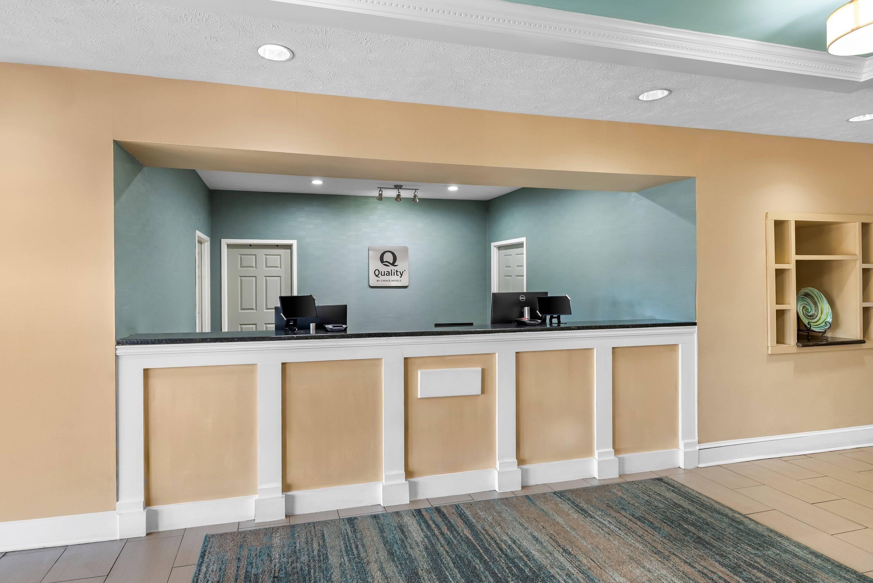 A reception desk with a 'Quality' sign, two computer stations, and a light-colored carpet.