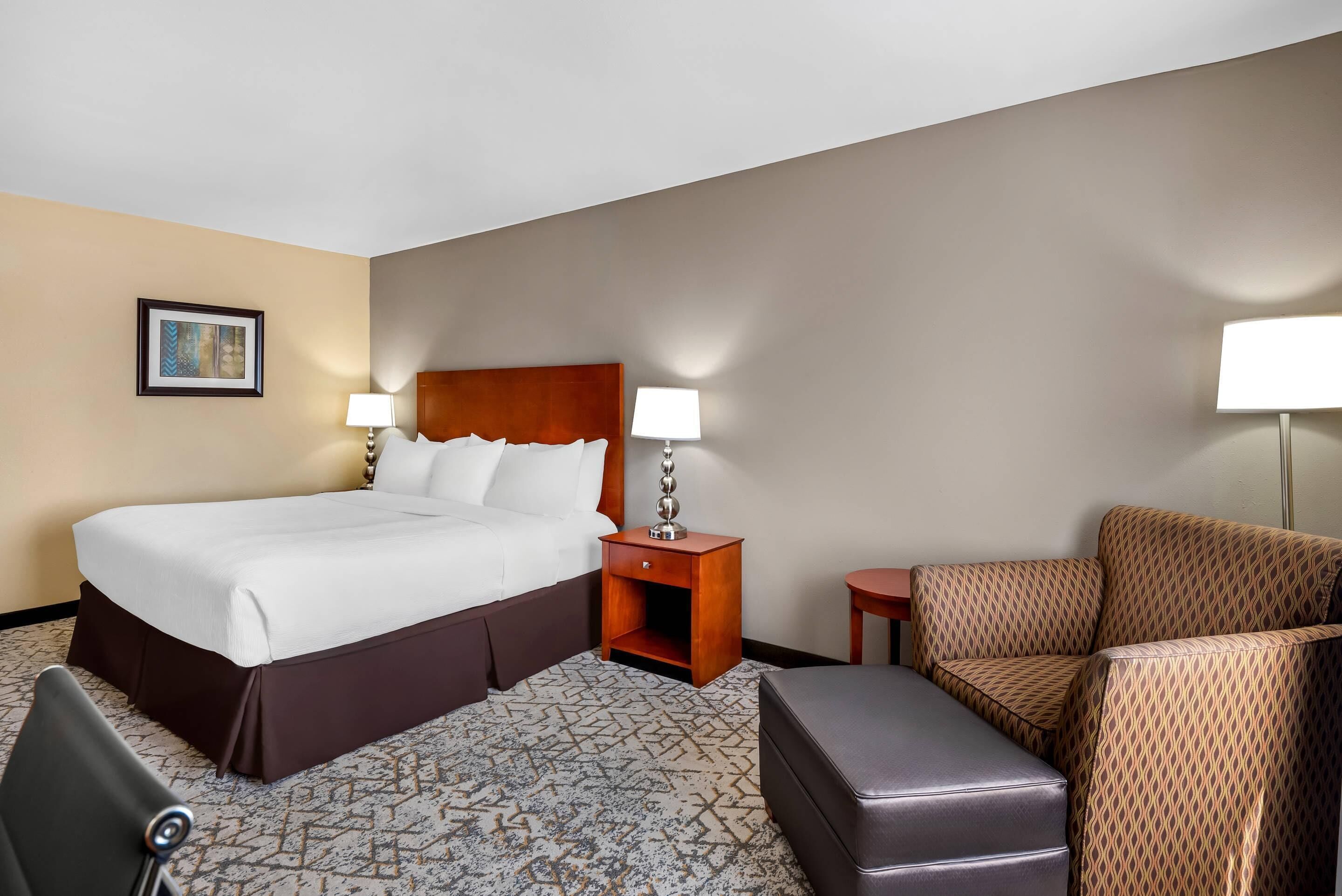 A hotel room with a large bed, two bedside tables with lamps, a patterned sofa, and a carpeted floor.
