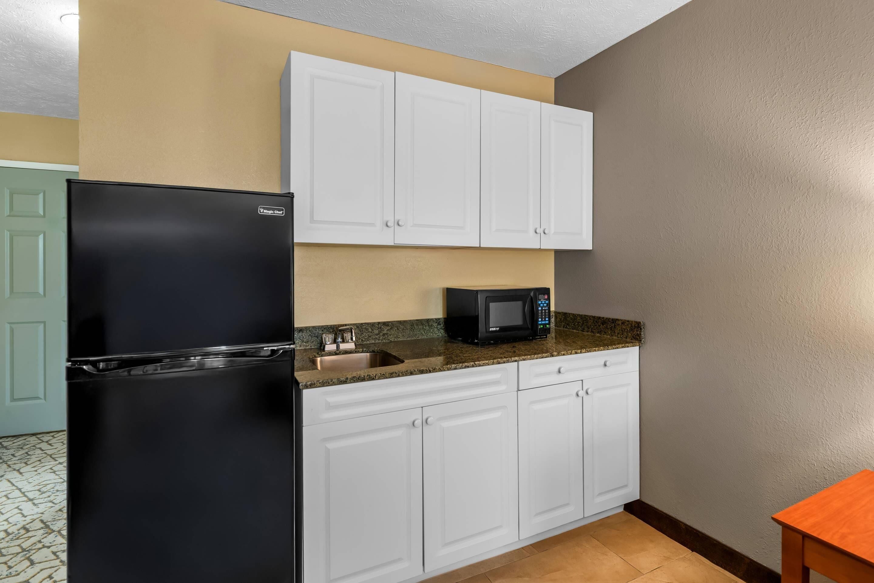 A kitchen with white cabinets, a black refrigerator, a microwave, and a granite countertop.