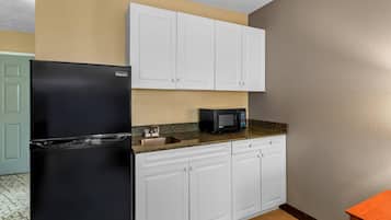Una cocina con armarios blancos, un refrigerador negro, un microondas y una encimera de granito.