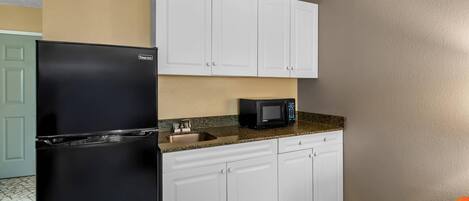 A kitchen with white cabinets, a black refrigerator, a microwave, and a granite countertop.