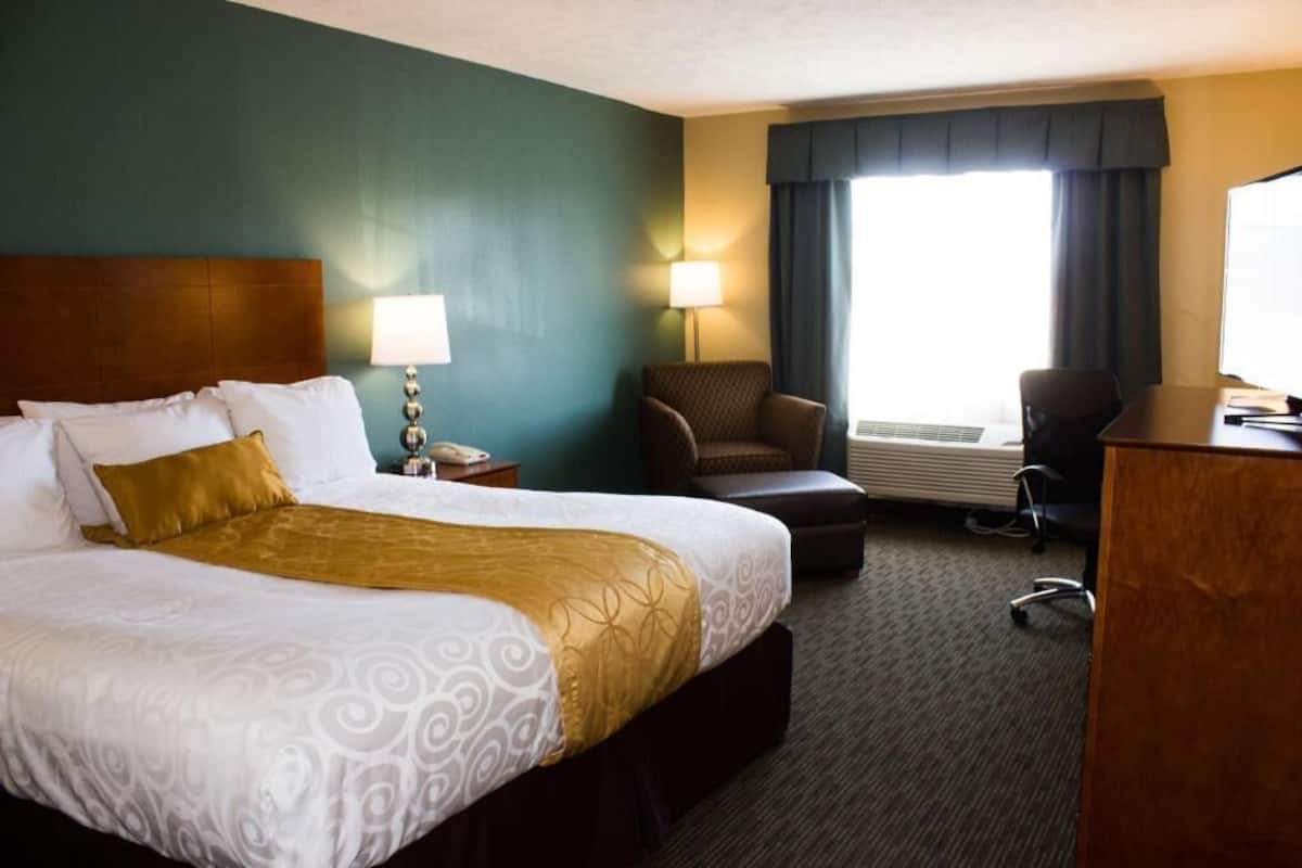 A hotel room with a large bed, a desk, a chair, and a window with curtains.