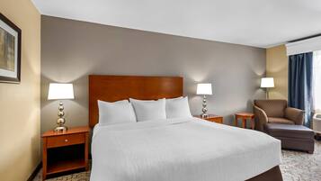 Ein Hotelzimmer mit einem großen Bett, zwei Nachttischen mit Lampen, einem Sessel und einem kleinen Tisch.