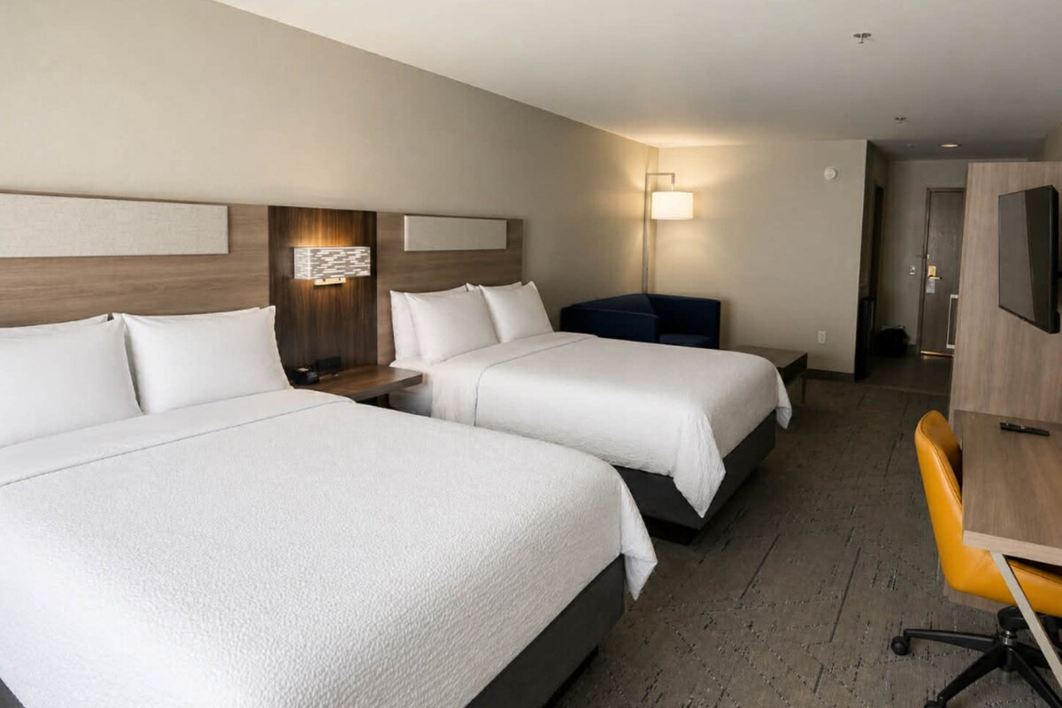 A hotel room with two beds, a desk, a chair, and a TV.