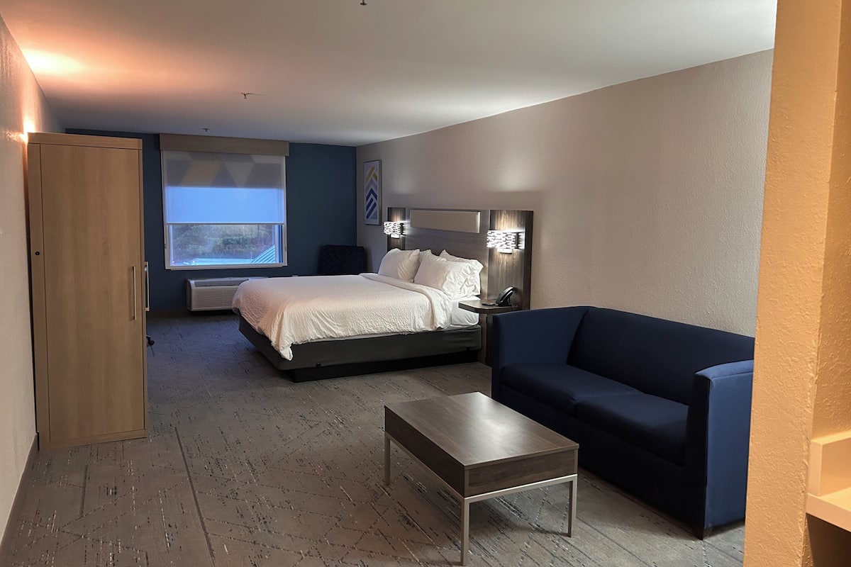 A hotel room with a bed, a sofa, a coffee table, a desk, and a window.