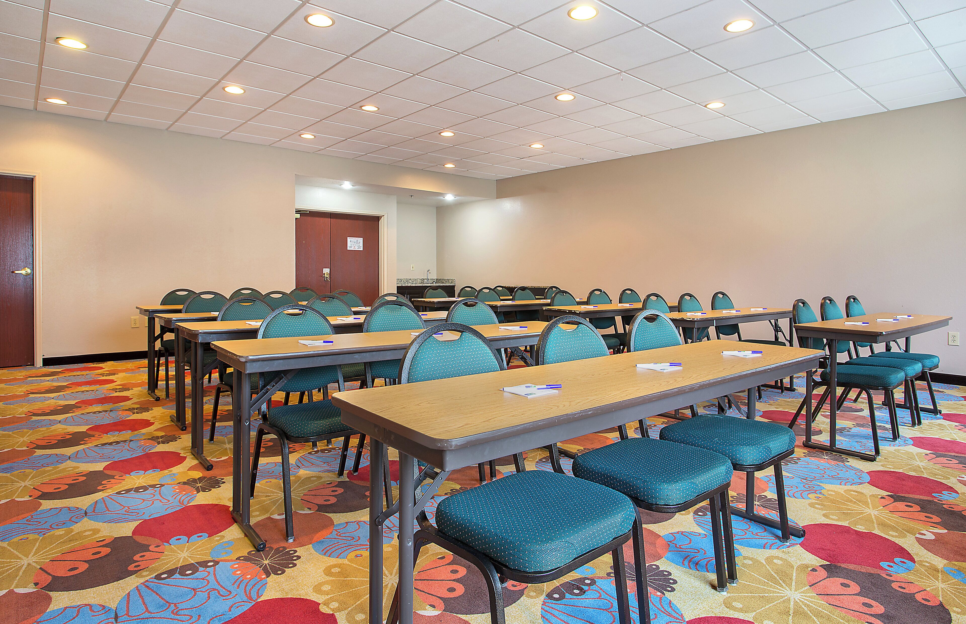 A conference room with tables and chairs, a kitchenette, and a door.