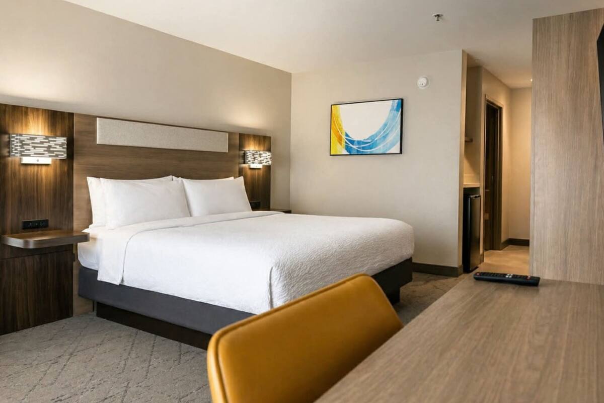 A hotel room with a bed, bedside tables, a desk, a chair, and a painting on the wall.