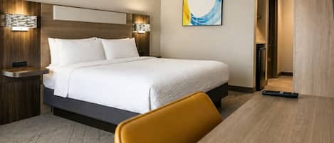 Ein Hotelzimmer mit Bett, Nachttischen, einem Schreibtisch, einem Sessel und einem Bild an der Wand.