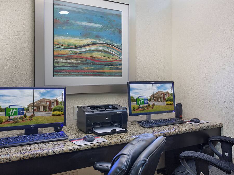 Una mesa de recepción de hotel con tres monitores mostrando el exterior del hotel, una impresora y un teclado.