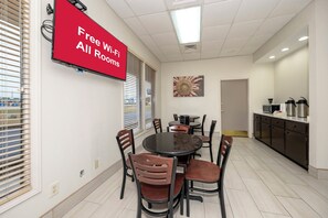 A conference room with a round table, chairs, a TV screen, and a painting on the wall. - Red Roof Inn Bay Minette (Bay Minette)