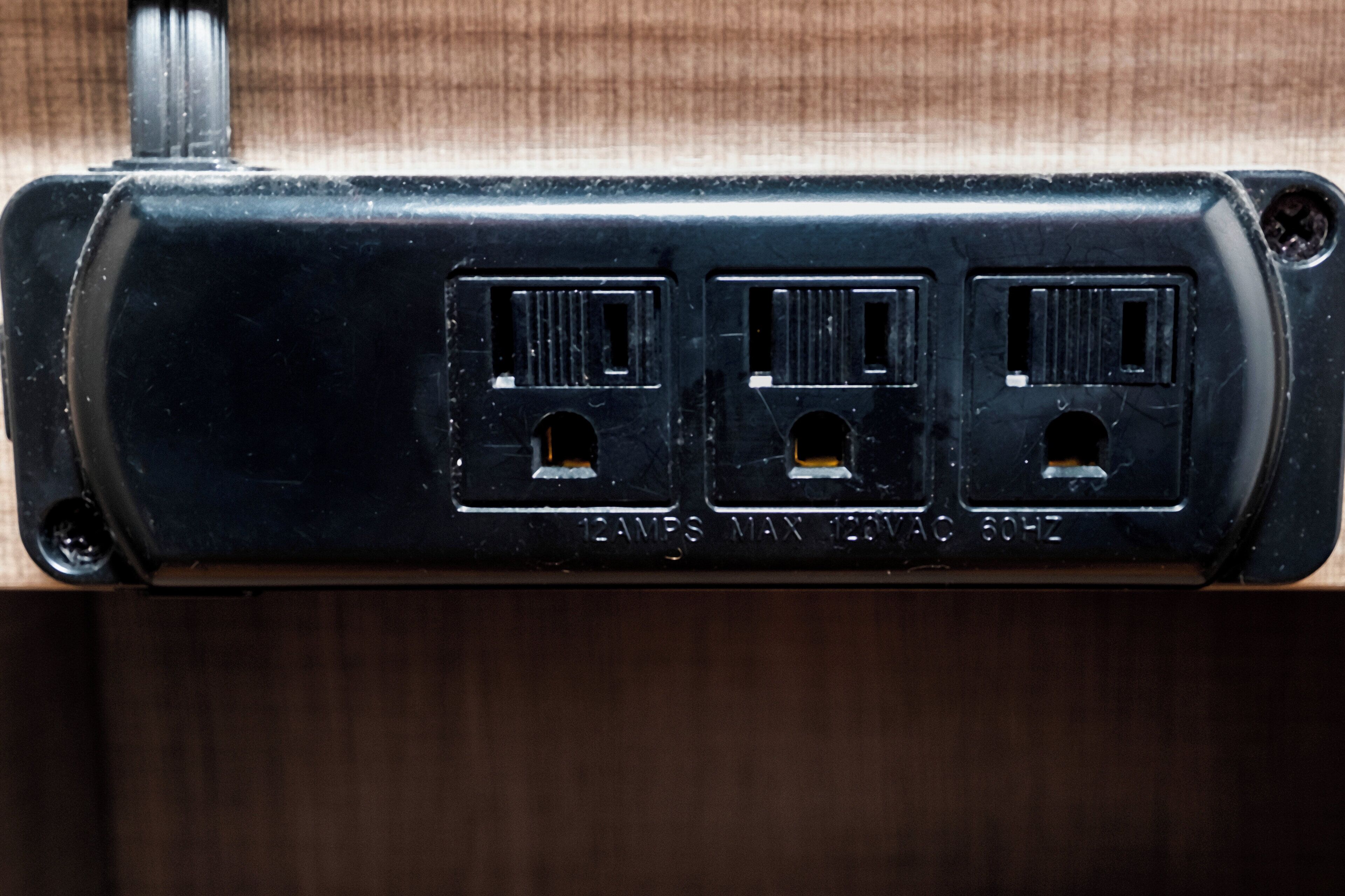 A black electrical outlet with three ports, labeled '12AMP MAX 120VAC 60HZ'.