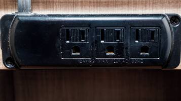 A black electrical outlet with three ports, labeled '12AMP MAX 120VAC 60HZ'.
