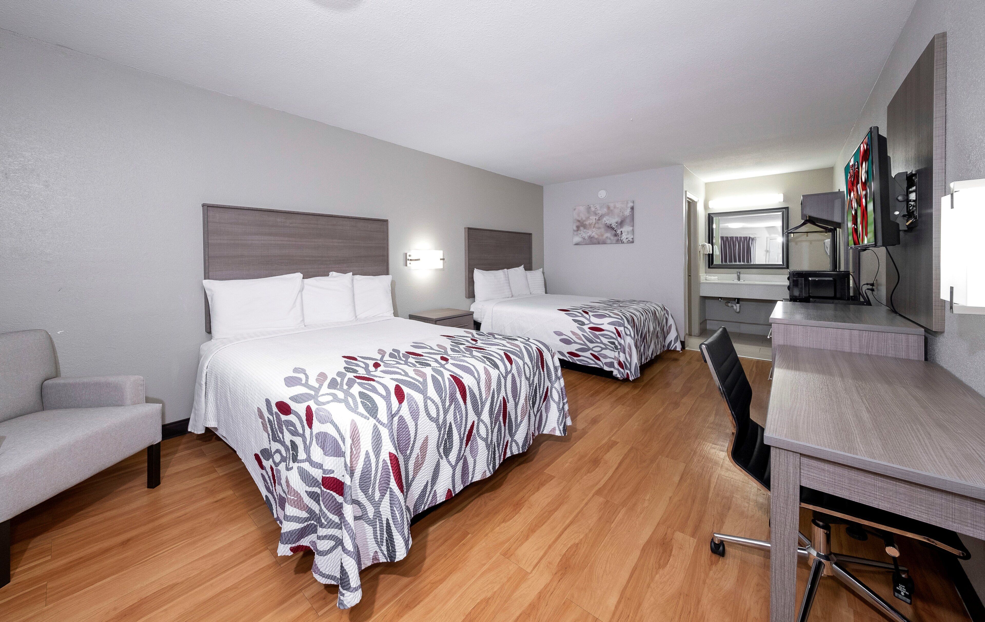 A hotel room with two beds, a desk, a chair, a mirror, and a television.
