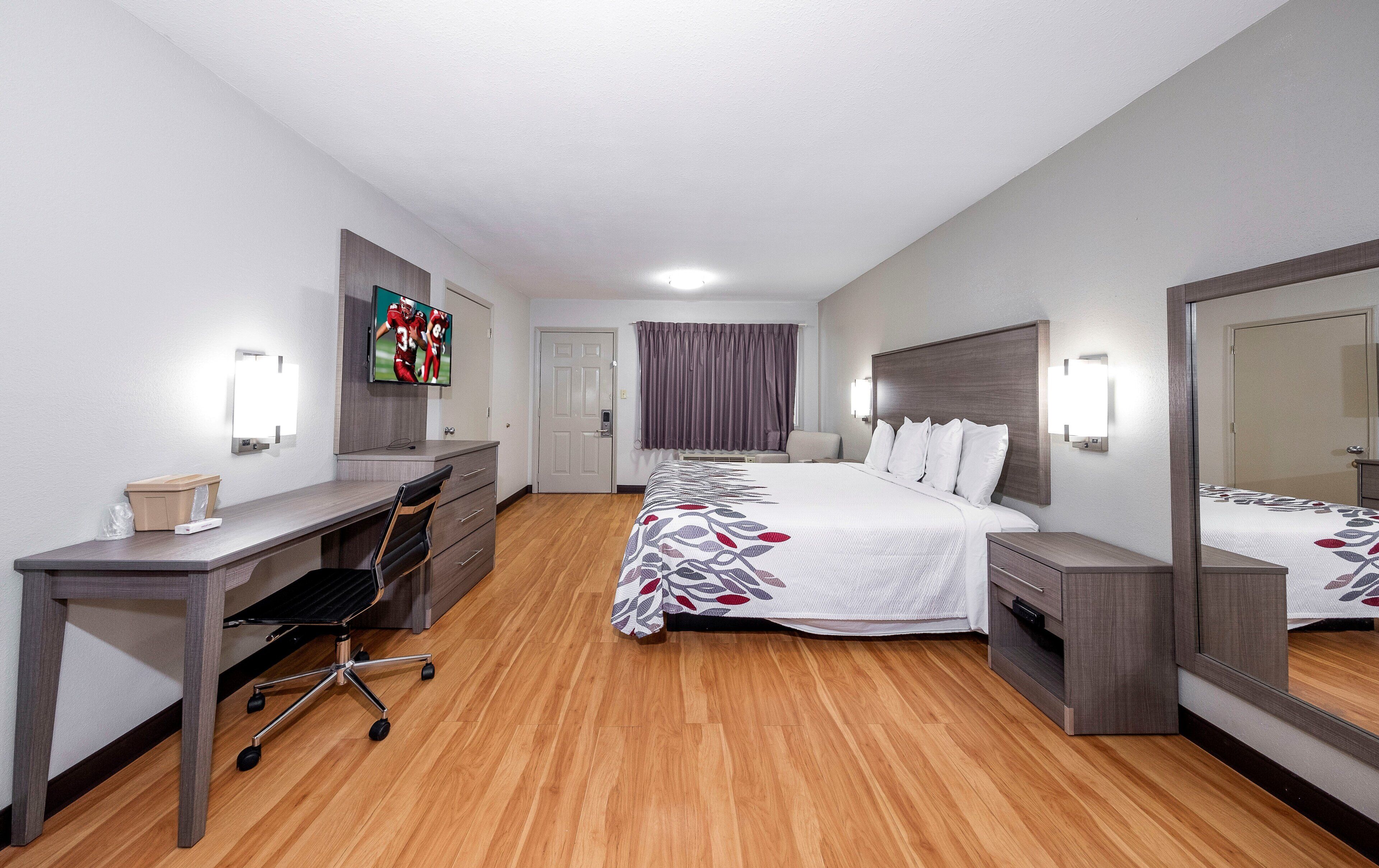Ein Hotelzimmer mit Bett, Nachttischen, Schreibtisch, Stuhl, Fernseher und Spiegel.