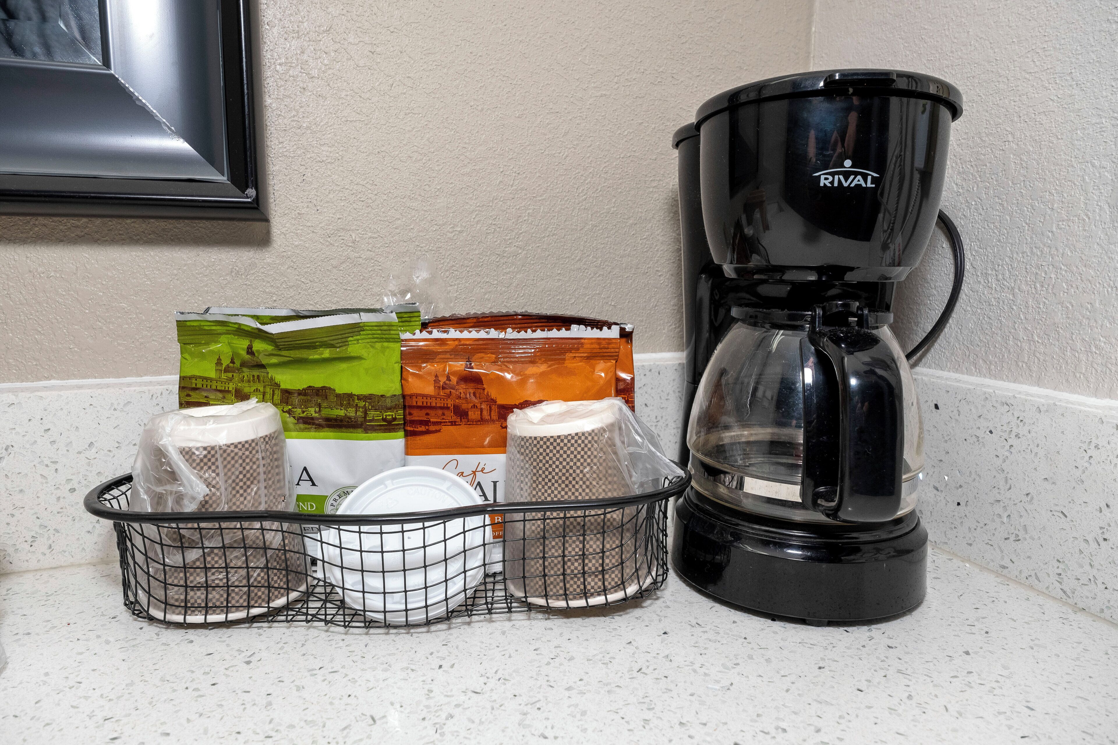 Un comptoir de cuisine avec une machine à café, un panier rempli de tasses et quelques aliments emballés.