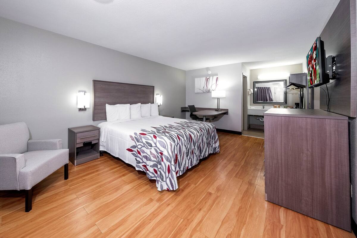 A hotel room with a bed, a desk, a chair, a small table, and a TV.