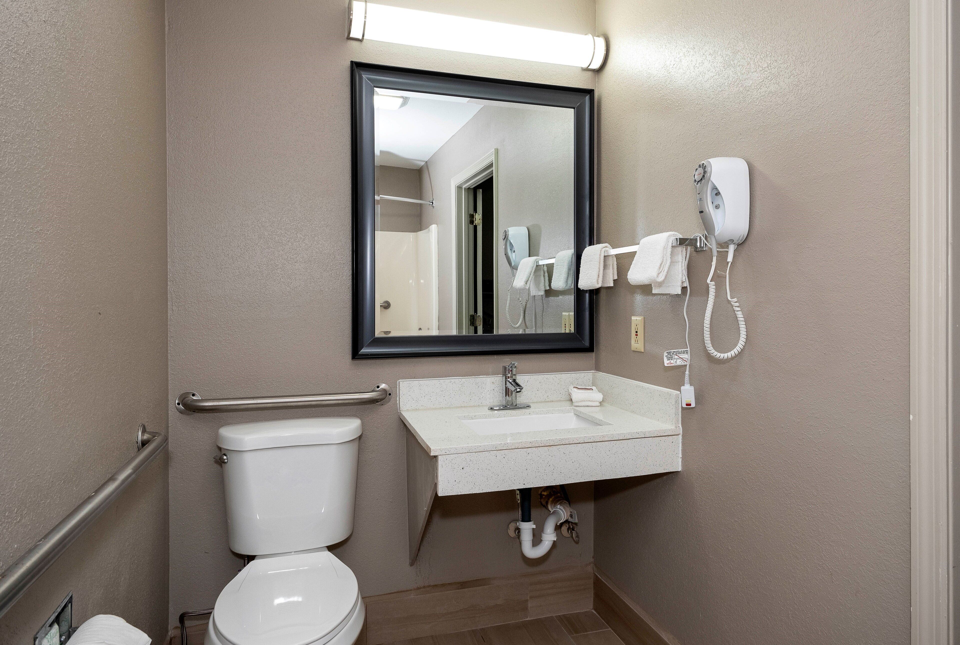 Un baño con inodoro, lavabo y secador de pelo sujeto a la pared.