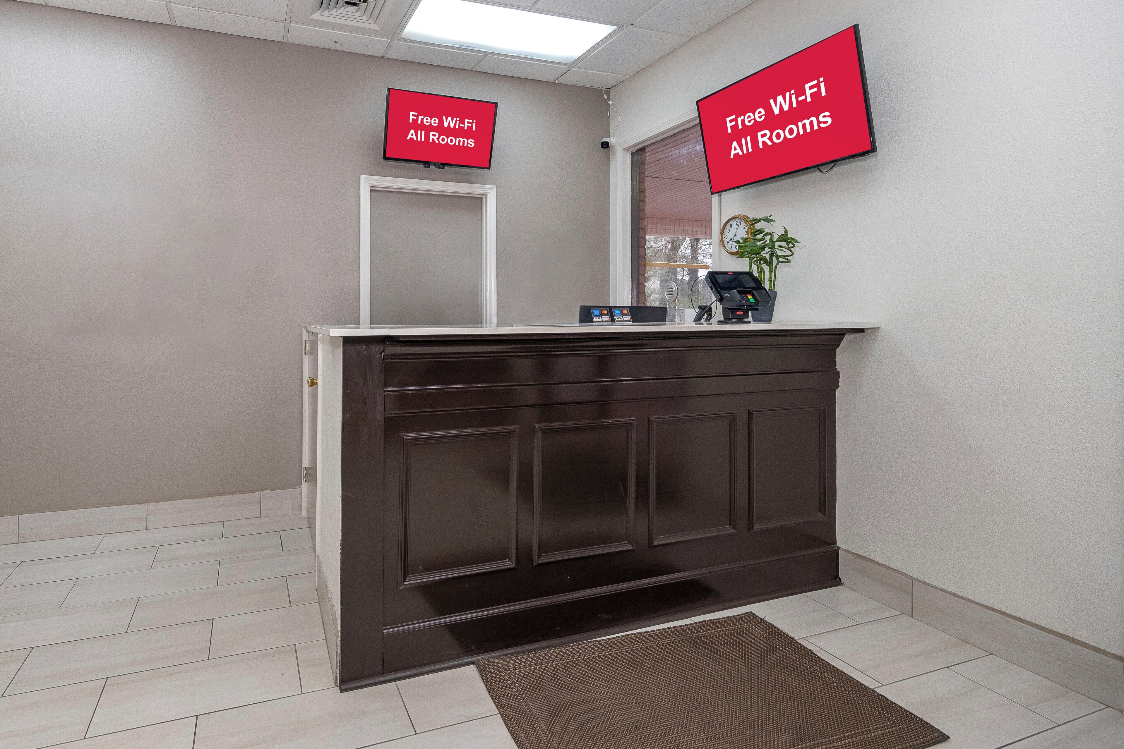 A reception area with a dark wood reception desk, a plant, and a clock on the wall.