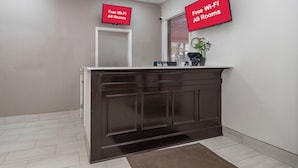 A reception area with a dark wood reception desk, a plant, and a clock on the wall. - Red Roof Inn Bay Minette (Bay Minette)