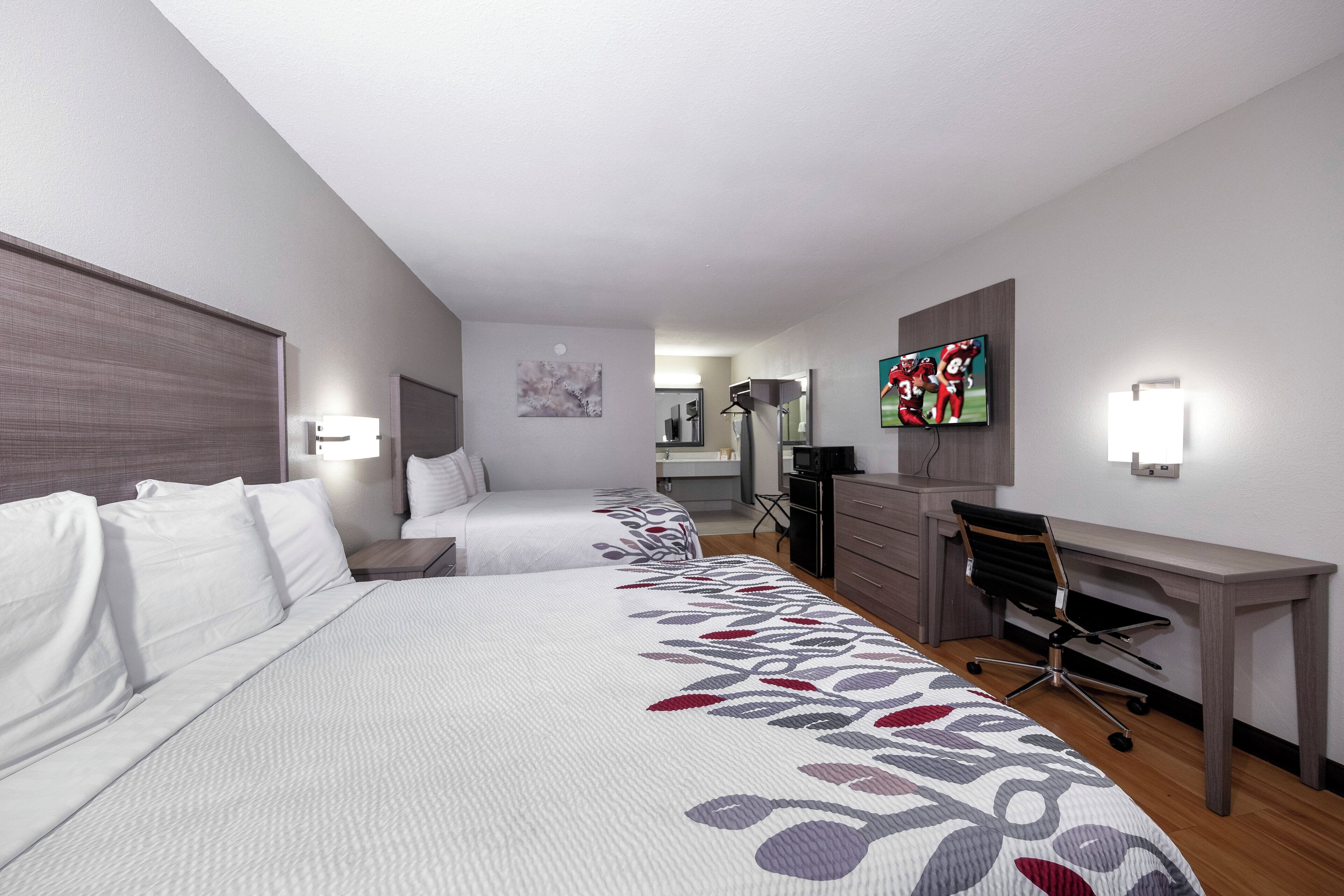 Une chambre d’hôtel avec deux lits, un bureau, une chaise, une télévision et, au fond, une salle de bain.