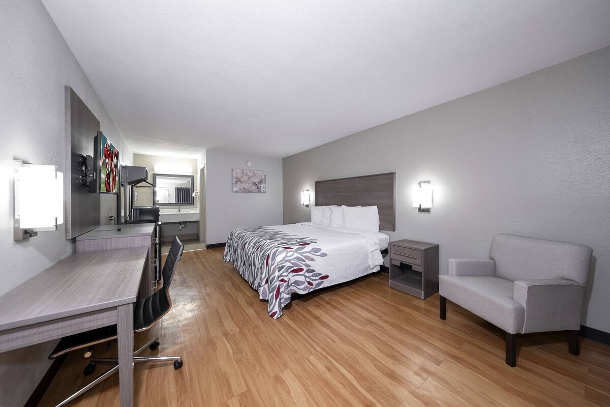 A hotel room with a bed, desk, chair, bedside table, and a sofa.