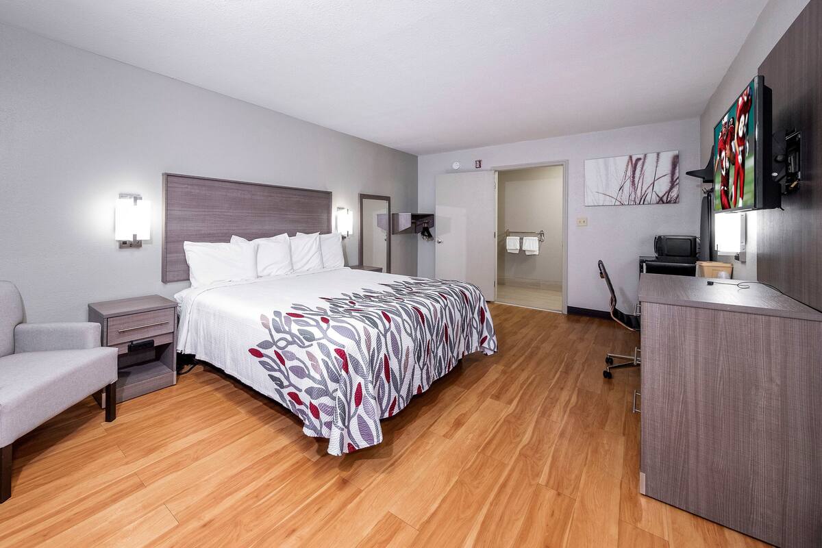 A modern hotel room with a large bed, a desk, a chair, and a wardrobe.