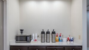 A kitchenette with a microwave, coffee makers, and various coffee and creamer containers.
