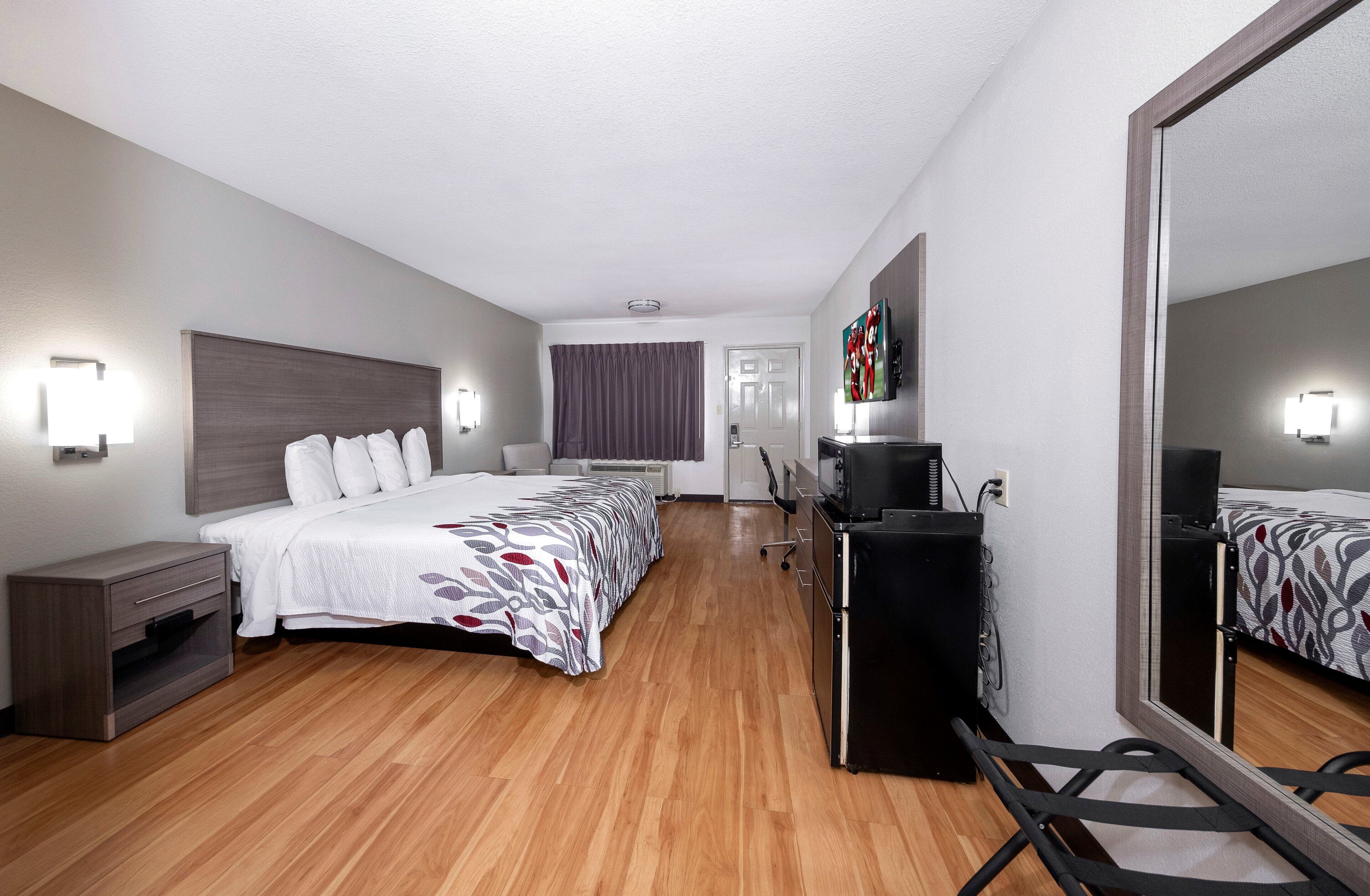 A hotel room with a bed, bedside tables, a desk, a TV, and a mirror.