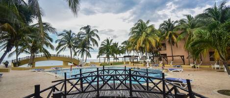 A pool area with a wooden deck, palm trees, and a bridge.