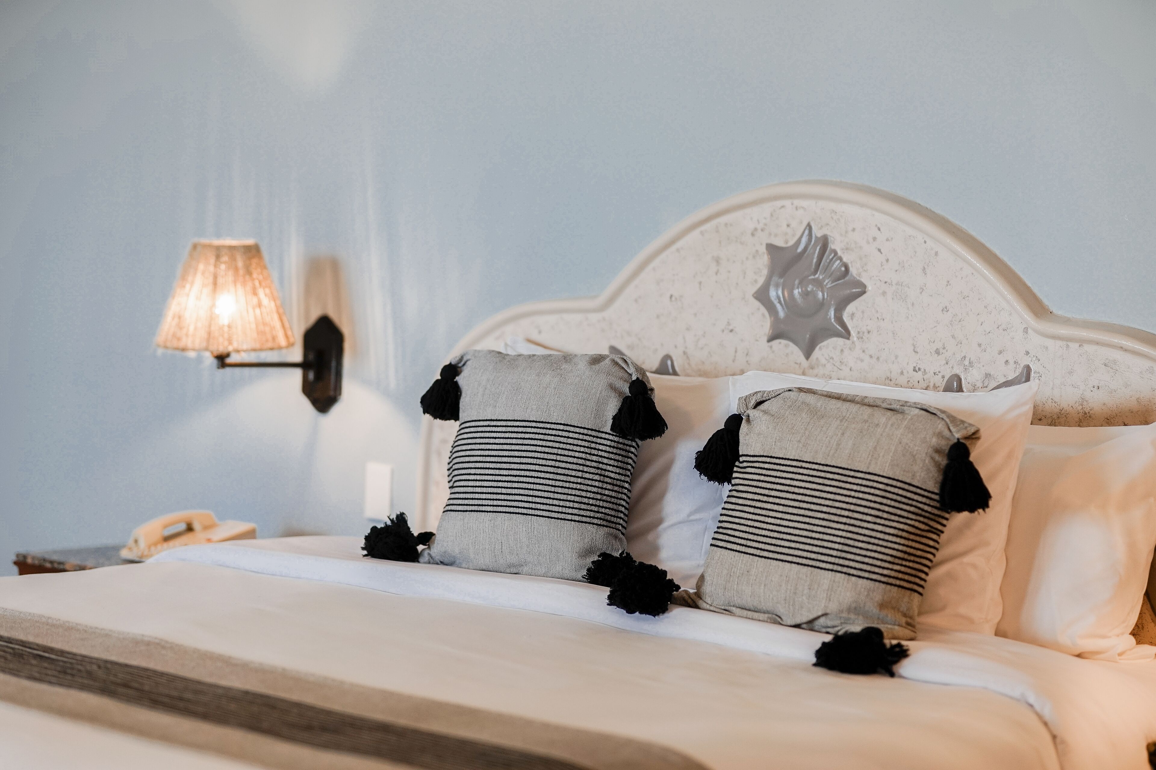 A neatly made bed with striped pillows and a decorative headboard, a bedside lamp, and a telephone on the nightstand.