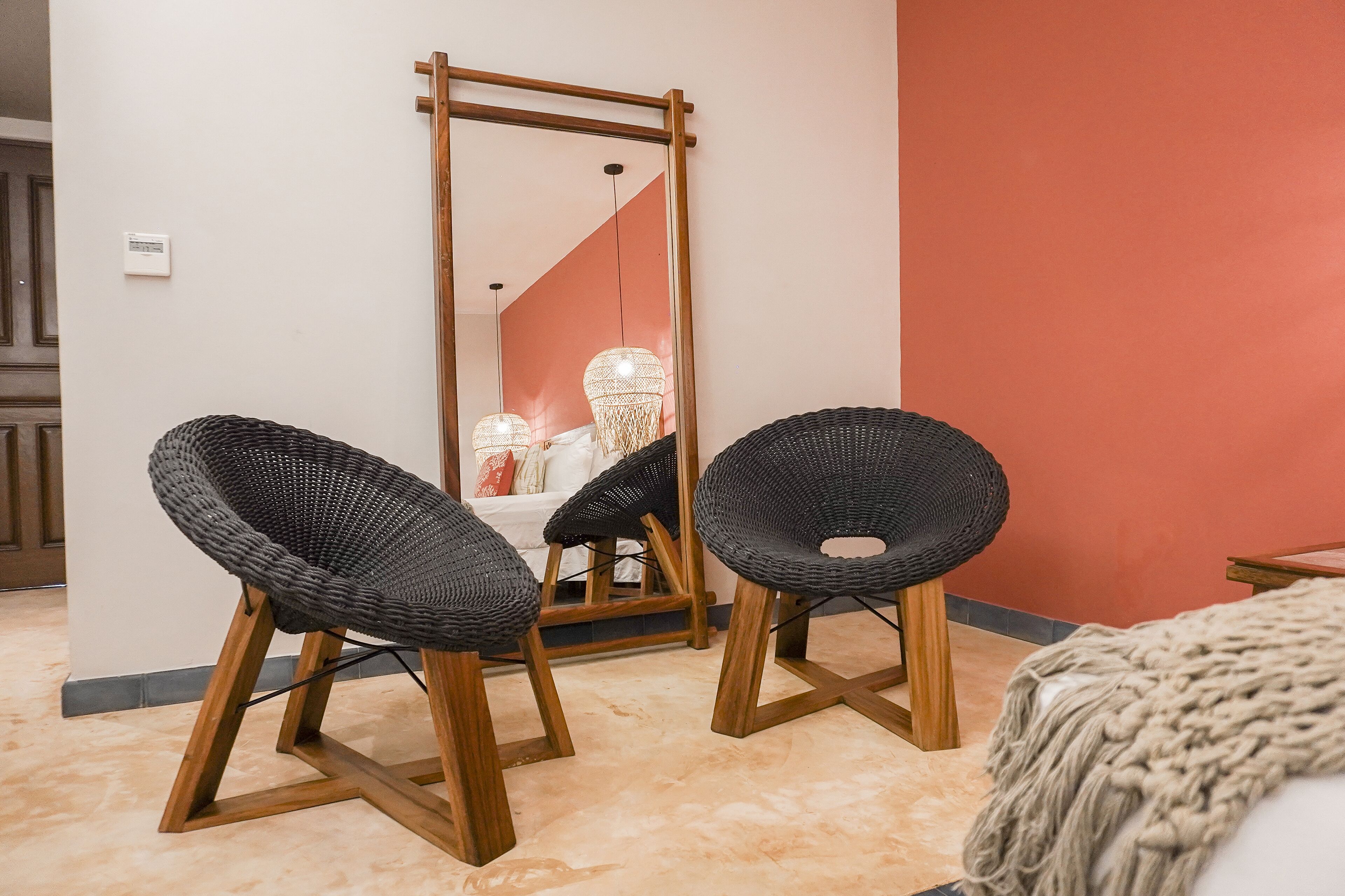 A room with two black woven chairs with wooden legs, a wooden-framed mirror, and a red wall.
