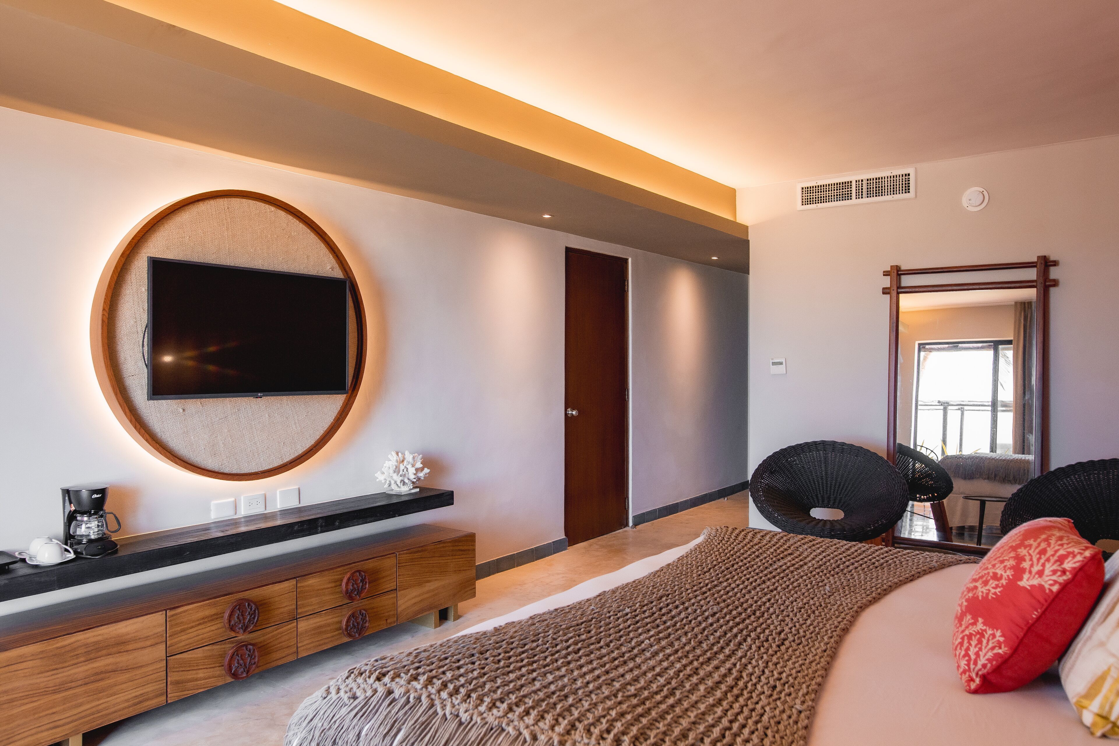A modern bedroom with a large bed, a round TV on the wall, a wooden dresser, and a large mirror.