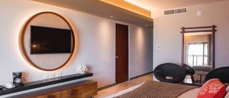 A modern bedroom with a large bed, a round TV on the wall, a wooden dresser, and a large mirror.