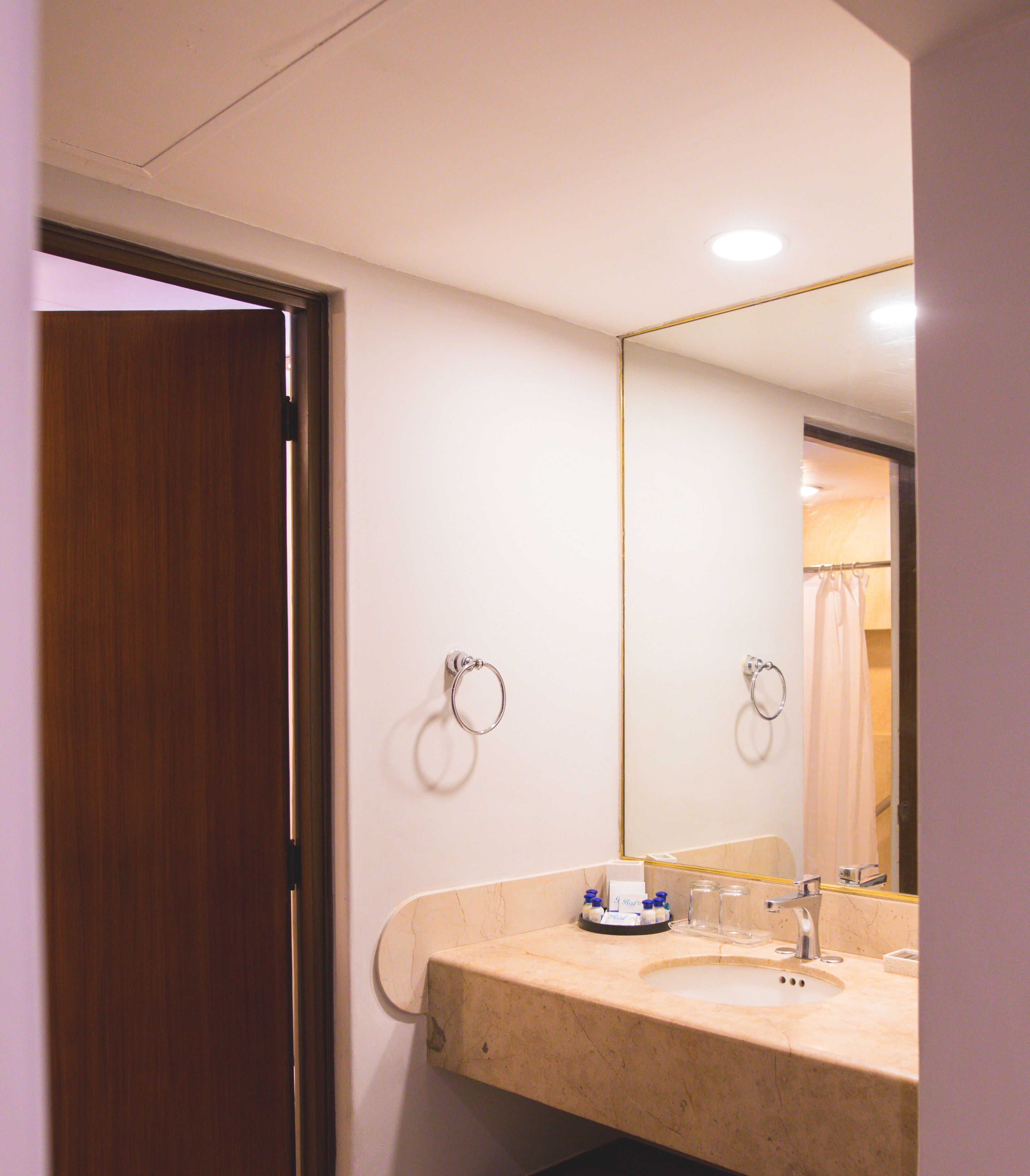 A bathroom with a sink, mirror, towel rings, and a shower curtain.